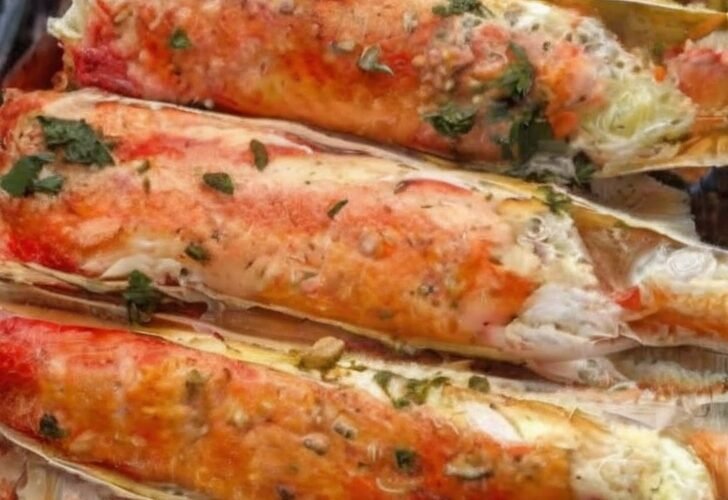 A close-up platter of baked king crab legs coated in rich garlic butter and Creole seasoning, garnished with fresh herbs and served with lemon wedges and a small dish of melted butter for dipping.