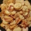A close-up of crispy golden potato slices and caramelized onions sizzling together in a skillet, with browned edges, tender centers, and a rustic homemade appearance.