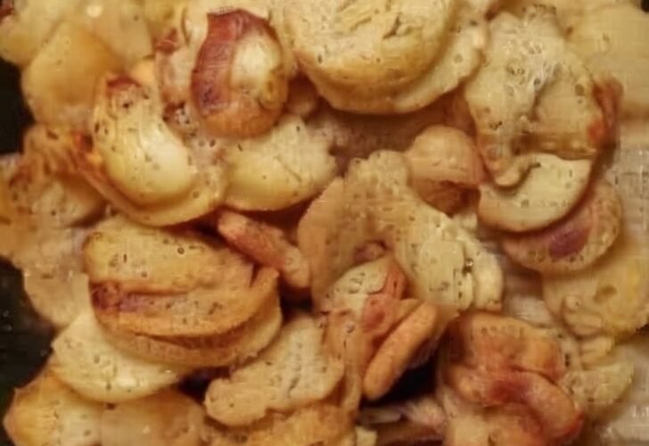 A close-up of crispy golden potato slices and caramelized onions sizzling together in a skillet, with browned edges, tender centers, and a rustic homemade appearance.