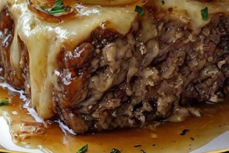 Crockpot French Onion Meatloaf with melted Swiss cheese, caramelized onions, savory onion gravy, and fresh parsley, served as a thick, tender slice on a plate.
