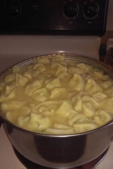 A large pot filled with creamy chicken and dumplings, featuring tender homemade dumplings simmering in a rich, savory broth on a stovetop.
