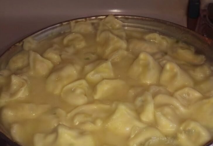 A large pot filled with creamy chicken and dumplings, featuring tender homemade dumplings simmering in a rich, savory broth on a stovetop.