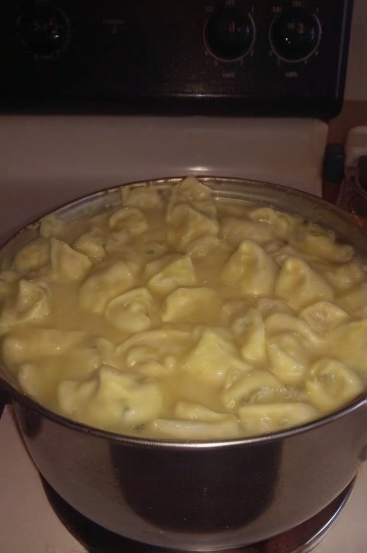 A large pot filled with creamy chicken and dumplings, featuring tender homemade dumplings simmering in a rich, savory broth on a stovetop.