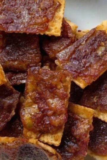 Close-up of homemade bacon-wrapped crackers stacked on a plate, featuring crisp golden crackers covered with caramelized brown sugar and smoky bacon.