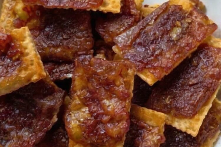 Close-up of homemade bacon-wrapped crackers stacked on a plate, featuring crisp golden crackers covered with caramelized brown sugar and smoky bacon.