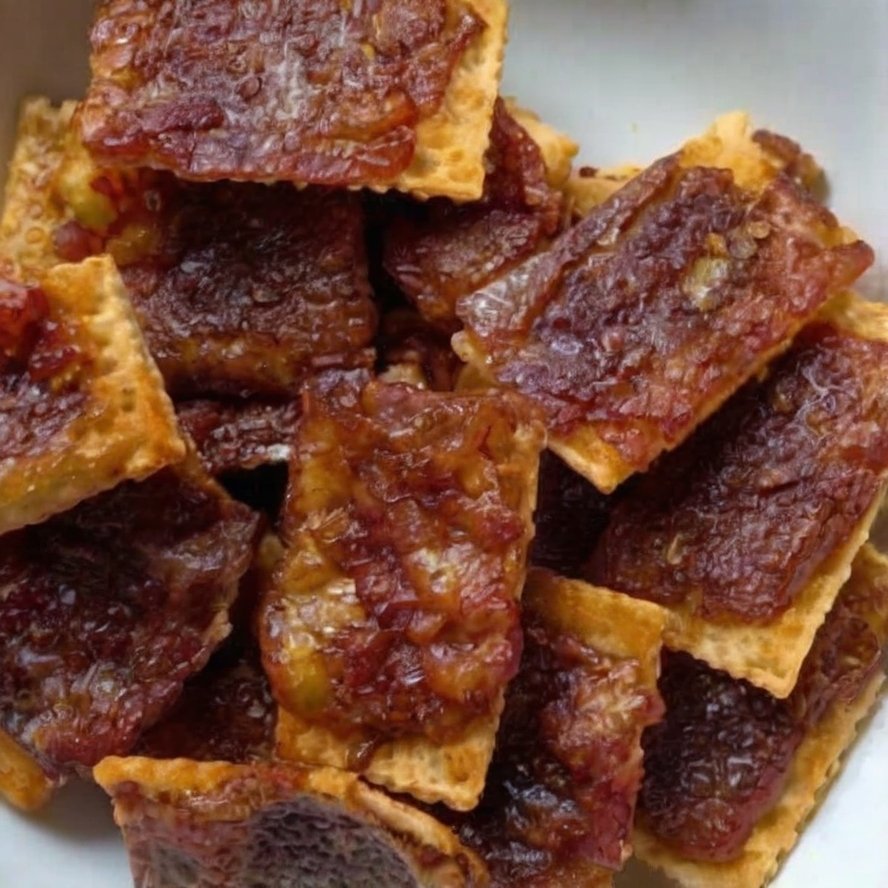 Close-up of homemade bacon-wrapped crackers stacked on a plate, featuring crisp golden crackers covered with caramelized brown sugar and smoky bacon.