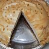 A homemade chocolate meringue pie in a foil pan, topped with a thick layer of golden-brown meringue and caramelized droplets, with a slice removed to reveal the rich chocolate filling and crust underneath.