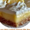 A close-up of a creamy lemon pie bar with a buttery golden crumb crust, topped with fluffy whipped cream and a fresh lemon slice. The lemon filling is smooth, bright yellow, and slightly glossy, with powdered sugar dusted around the edges.