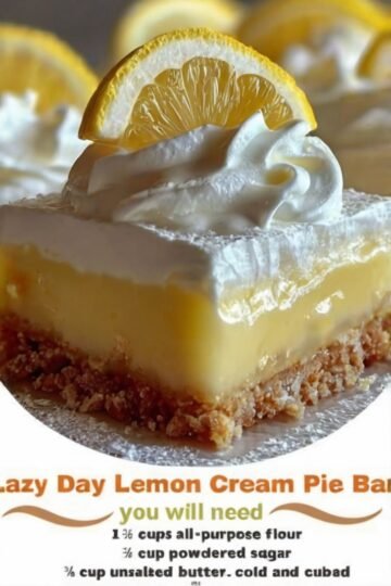 A close-up of a creamy lemon pie bar with a buttery golden crumb crust, topped with fluffy whipped cream and a fresh lemon slice. The lemon filling is smooth, bright yellow, and slightly glossy, with powdered sugar dusted around the edges.