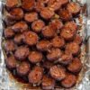 A tray of sliced kielbasa sausage bites coated in a glossy, dark caramelized brown sugar glaze. The sausage pieces are deeply browned and slightly crisp around the edges, with a sticky, shiny coating.