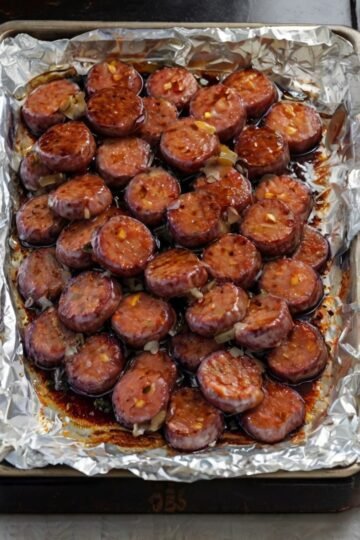 A tray of sliced kielbasa sausage bites coated in a glossy, dark caramelized brown sugar glaze. The sausage pieces are deeply browned and slightly crisp around the edges, with a sticky, shiny coating.