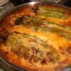 Baked chile rellenos casserole topped with melted golden cheese, featuring roasted poblano peppers nestled in a creamy egg-and-cheese mixture inside a round baking dish.