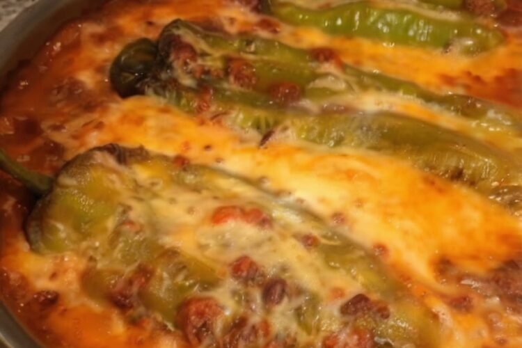Baked chile rellenos casserole topped with melted golden cheese, featuring roasted poblano peppers nestled in a creamy egg-and-cheese mixture inside a round baking dish.