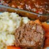 Home-cooked meatloaf with mashed potatoes, carrots, and savory tomato sauce served on a white plate.