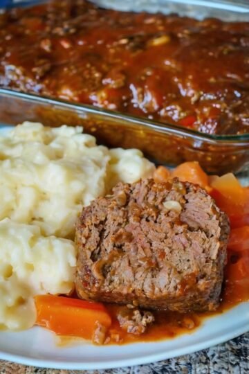 Home-cooked meatloaf with mashed potatoes, carrots, and savory tomato sauce served on a white plate.