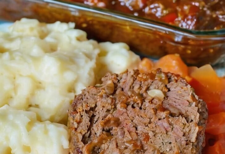 Home-cooked meatloaf with mashed potatoes, carrots, and savory tomato sauce served on a white plate.