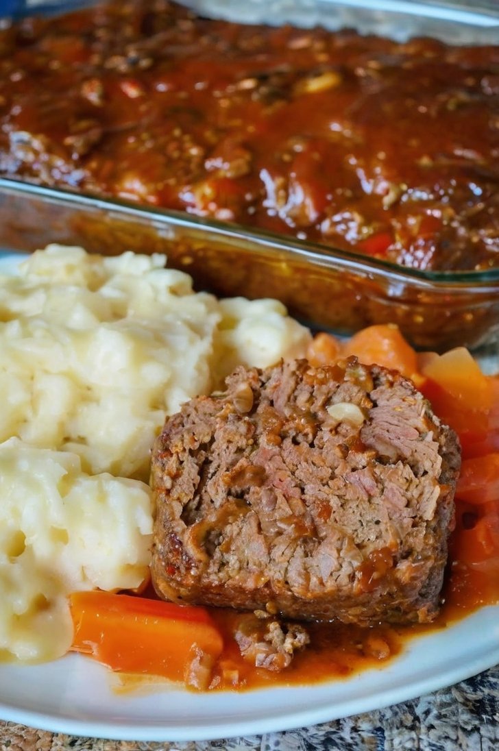 Home-cooked meatloaf with mashed potatoes, carrots, and savory tomato sauce served on a white plate.