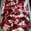 A rectangular tray of Heaven on Earth Cake layered with fluffy cake, creamy white pudding, whipped topping, and swirls of glossy cherry pie filling across the top.