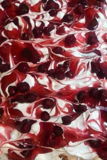 A rectangular tray of Heaven on Earth Cake layered with fluffy cake, creamy white pudding, whipped topping, and swirls of glossy cherry pie filling across the top.