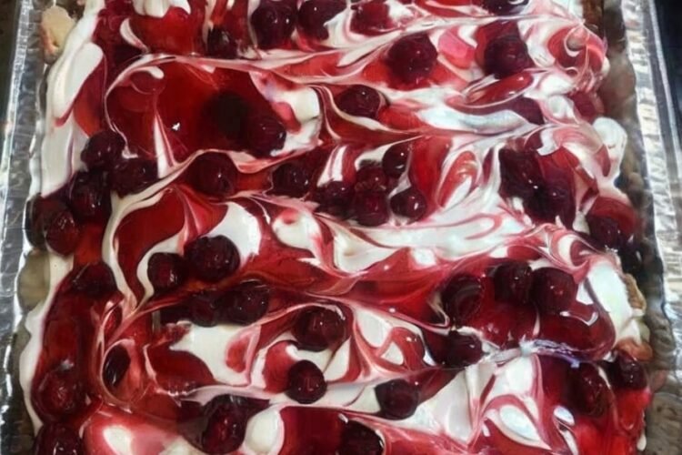 A rectangular tray of Heaven on Earth Cake layered with fluffy cake, creamy white pudding, whipped topping, and swirls of glossy cherry pie filling across the top.
