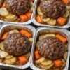 Four individual meatloaf portions baked in aluminum trays with sliced potatoes and carrots, topped with a savory brown glaze.