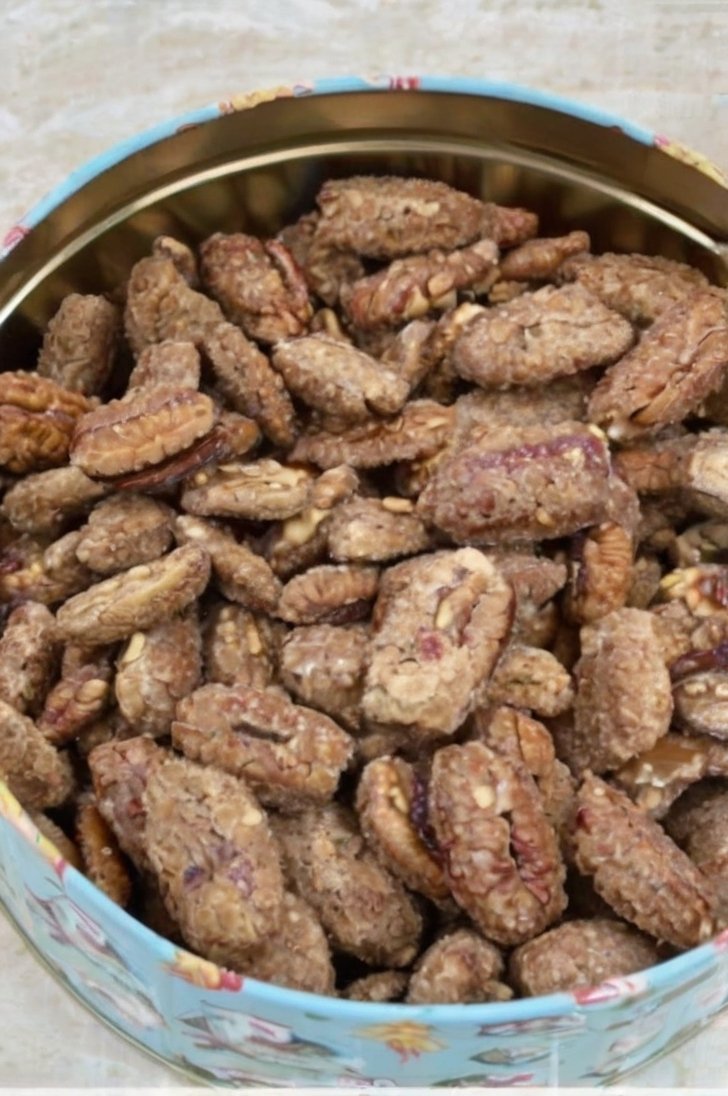 A round decorative tin filled with homemade candied pecan halves coated in a crunchy cinnamon-sugar mixture.