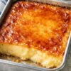 A rich baked custard dessert with a smooth, creamy golden center and a glossy caramelized top, baked in a rectangular metal pan and sliced into thick squares.
