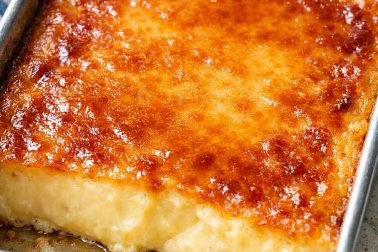 A rich baked custard dessert with a smooth, creamy golden center and a glossy caramelized top, baked in a rectangular metal pan and sliced into thick squares.