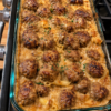 A baked meatball casserole filled with tender golden-brown meatballs in a rich, creamy sauce, arranged in a rectangular baking dish and finished with a lightly browned, savory topping.