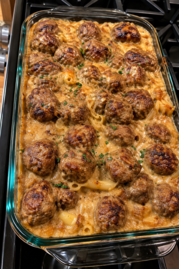 A baked meatball casserole filled with tender golden-brown meatballs in a rich, creamy sauce, arranged in a rectangular baking dish and finished with a lightly browned, savory topping.