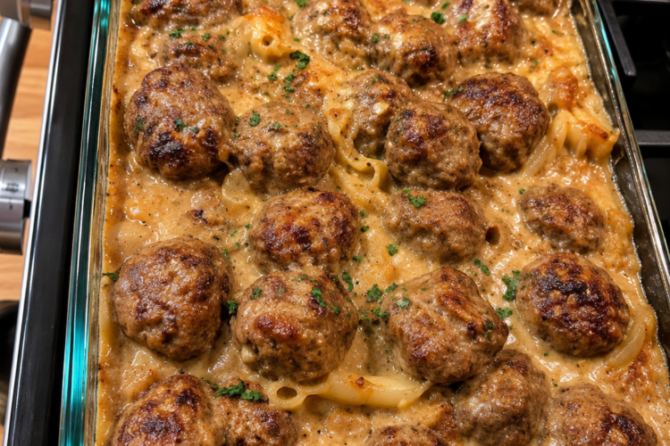 A baked meatball casserole filled with tender golden-brown meatballs in a rich, creamy sauce, arranged in a rectangular baking dish and finished with a lightly browned, savory topping.