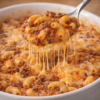 A spoonful of cheesy baked beef macaroni, featuring tender elbow pasta, seasoned ground beef, rich tomato sauce, and plenty of gooey melted cheese stretching from the casserole.