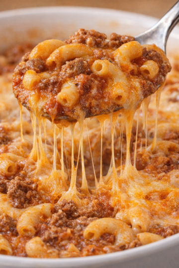 A spoonful of cheesy baked beef macaroni, featuring tender elbow pasta, seasoned ground beef, rich tomato sauce, and plenty of gooey melted cheese stretching from the casserole.