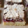 A close-up of raspberry crumble bars with a buttery golden shortbread base, a rich layer of raspberry filling, and a crumbly, lightly browned topping.