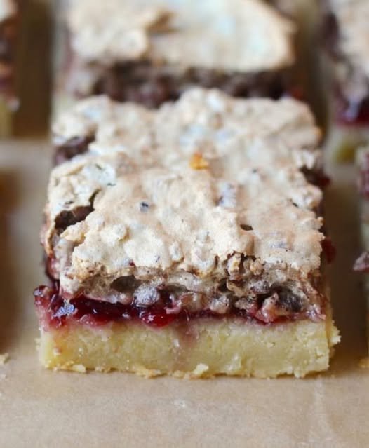 A close-up of raspberry crumble bars with a buttery golden shortbread base, a rich layer of raspberry filling, and a crumbly, lightly browned topping.