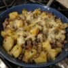 A hearty skillet of golden crispy potato cubes and seasoned ground beef topped with melted cheese, garnished with herbs and served hot.