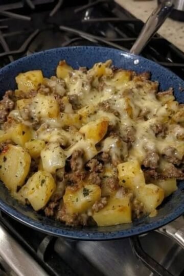 A hearty skillet of golden crispy potato cubes and seasoned ground beef topped with melted cheese, garnished with herbs and served hot.