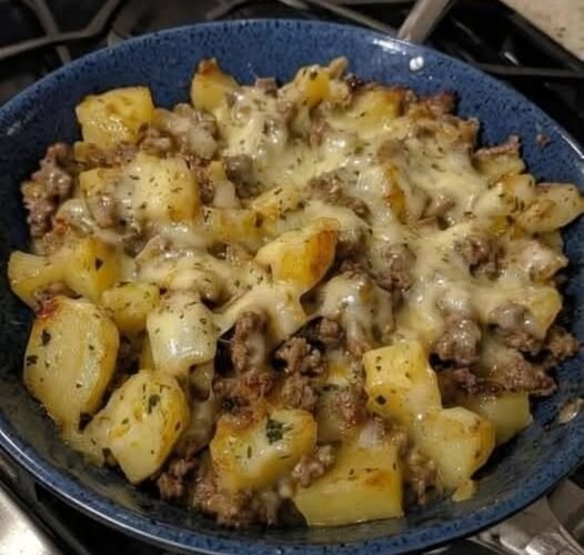 A hearty skillet of golden crispy potato cubes and seasoned ground beef topped with melted cheese, garnished with herbs and served hot.