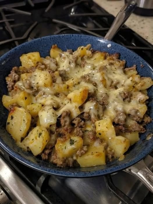 A hearty skillet of golden crispy potato cubes and seasoned ground beef topped with melted cheese, garnished with herbs and served hot.
