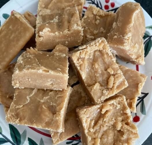 A plate of chunky, golden-brown peanut butter fudge squares with a rich, creamy texture and slightly crumbly edges.