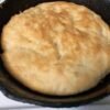 A large homemade skillet bread with a soft, fluffy center and a lightly golden, rustic crust, baked directly in a black cast-iron pan.