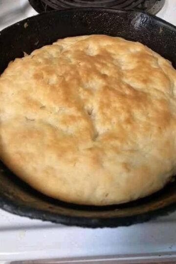 A large homemade skillet bread with a soft, fluffy center and a lightly golden, rustic crust, baked directly in a black cast-iron pan.