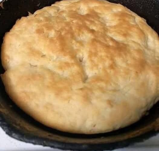 A large homemade skillet bread with a soft, fluffy center and a lightly golden, rustic crust, baked directly in a black cast-iron pan.