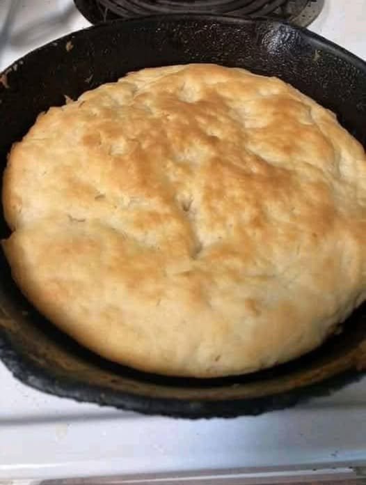 A large homemade skillet bread with a soft, fluffy center and a lightly golden, rustic crust, baked directly in a black cast-iron pan.