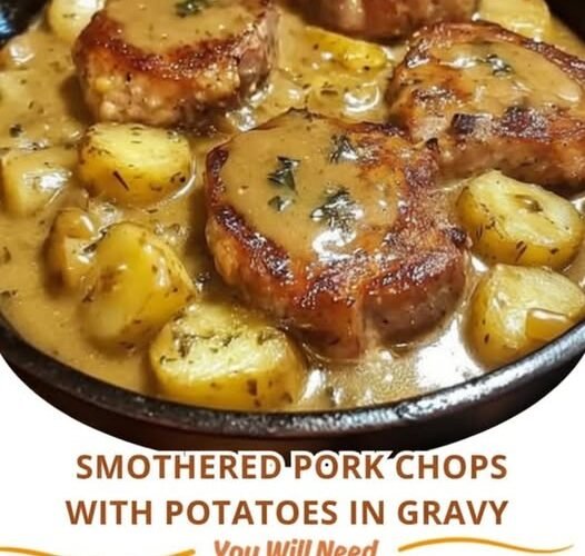 A comforting skillet of golden-browned smothered pork chops nestled among tender potatoes and coated in a rich, savory herb gravy.