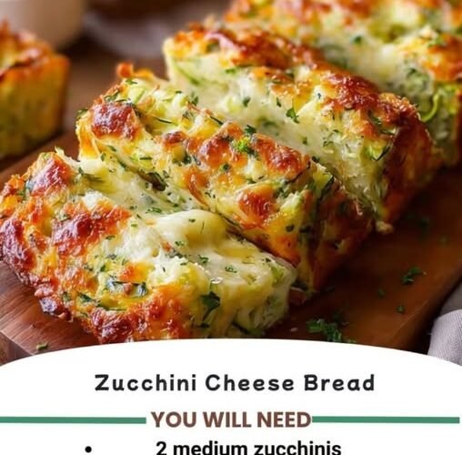 A golden, cheesy zucchini bread loaf with a crisp browned crust, tender zucchini-filled center, melted cheese throughout, and fresh herbs sprinkled on top.