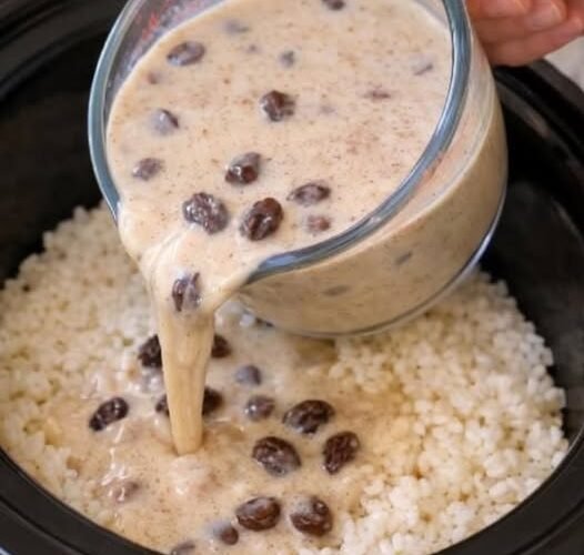 A creamy rice dish in a slow cooker, topped with a rich, velvety sauce studded with plump raisins, being poured over fluffy white rice.