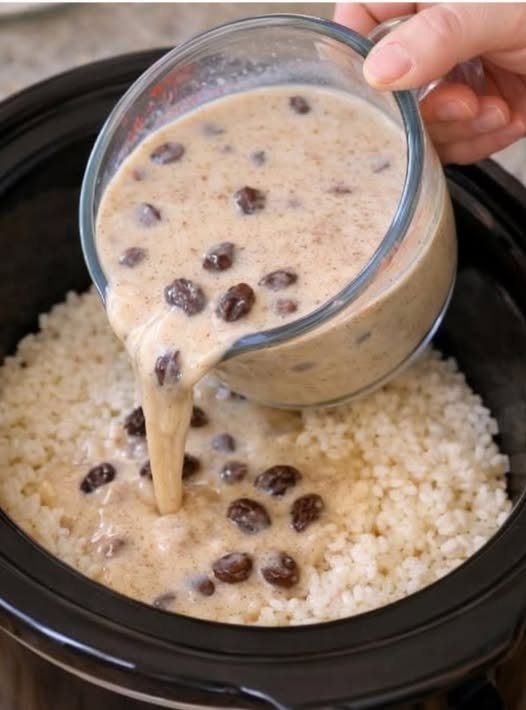 A creamy rice dish in a slow cooker, topped with a rich, velvety sauce studded with plump raisins, being poured over fluffy white rice.