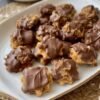 A plate of golden, chewy pecan cookies topped with rich melted chocolate, featuring crunchy chopped pecans and a soft, buttery center.