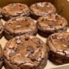 A box of thick, fudgy chocolate brownie cookies topped with plenty of semi-sweet chocolate chips, featuring crackly tops and rich, gooey centers